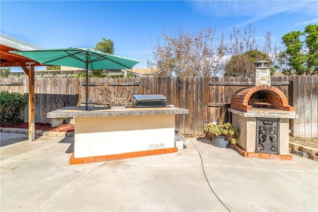 view of patio with an outdoor kitchen, fence private yard, an outdoor fireplace, and a grill