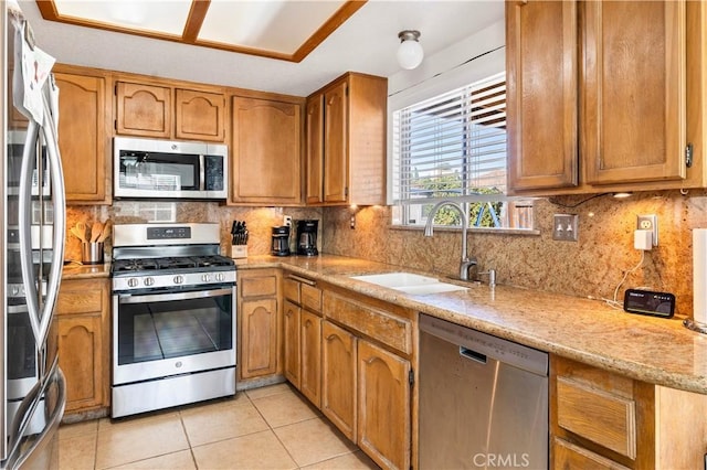 kitchen featuring light tile patterned flooring, stainless steel appliances, a sink, tasteful backsplash, and brown cabinetry