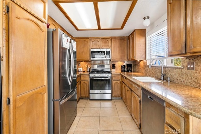 kitchen with light tile patterned floors, stainless steel appliances, a sink, backsplash, and brown cabinetry