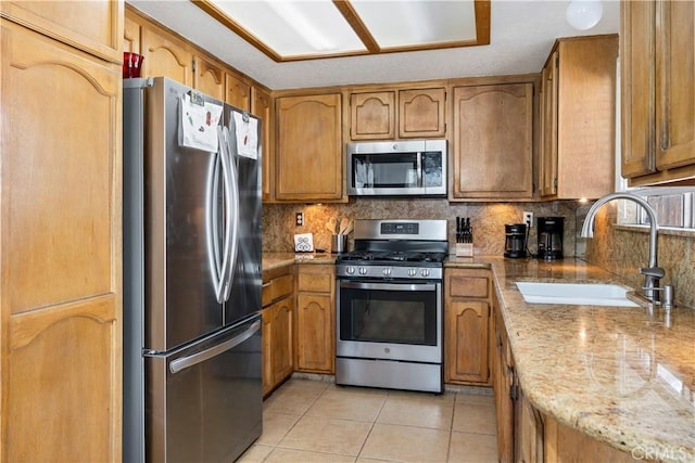 kitchen featuring light tile patterned floors, tasteful backsplash, appliances with stainless steel finishes, brown cabinets, and a sink