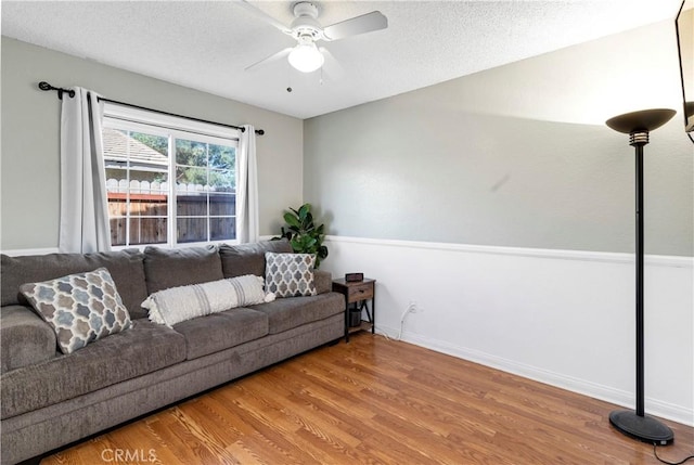 living area with ceiling fan, a textured ceiling, baseboards, and wood finished floors