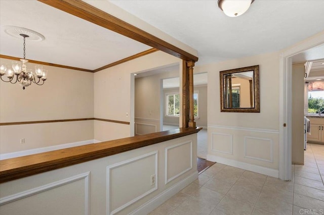 hallway featuring a wainscoted wall, crown molding, light tile patterned floors, a decorative wall, and a chandelier