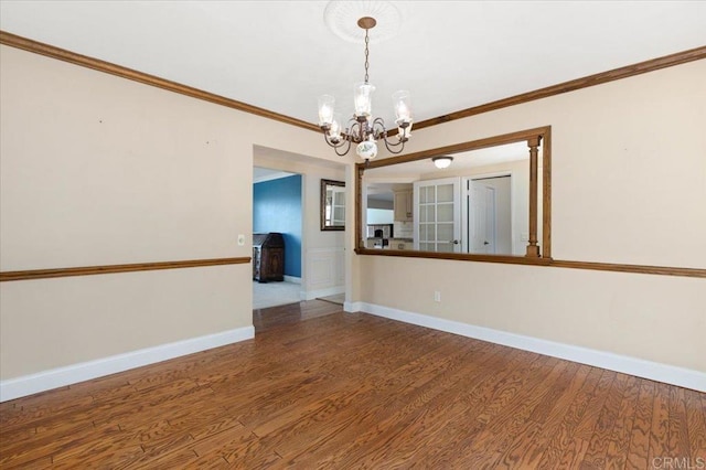 unfurnished room with a notable chandelier, crown molding, baseboards, and wood finished floors