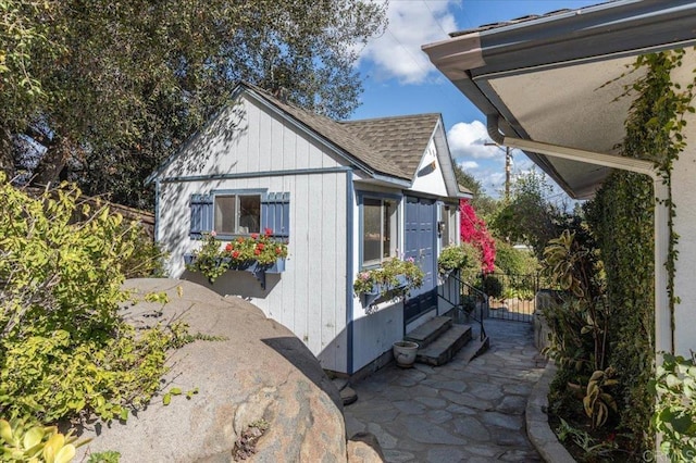 view of side of home with entry steps, fence, a patio, and roof with shingles