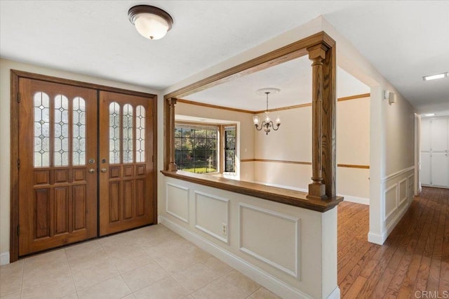 foyer with a chandelier, a decorative wall, a wainscoted wall, ornamental molding, and ornate columns