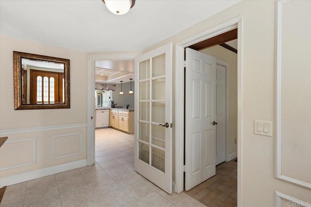 hallway with light tile patterned floors, a decorative wall, and wainscoting