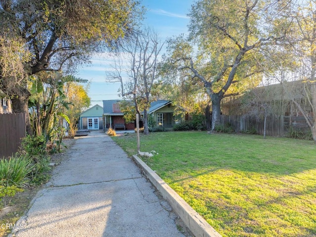 view of front facade with driveway, fence, a front lawn, and french doors