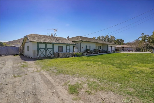 view of front of house with dirt driveway, a front lawn, and stucco siding