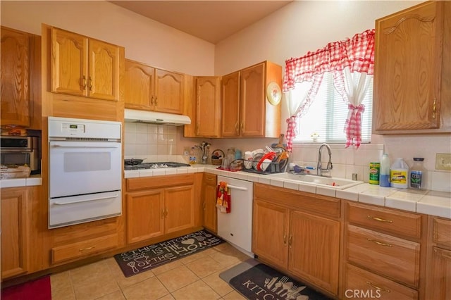 kitchen featuring white appliances, a sink, under cabinet range hood, backsplash, and a warming drawer