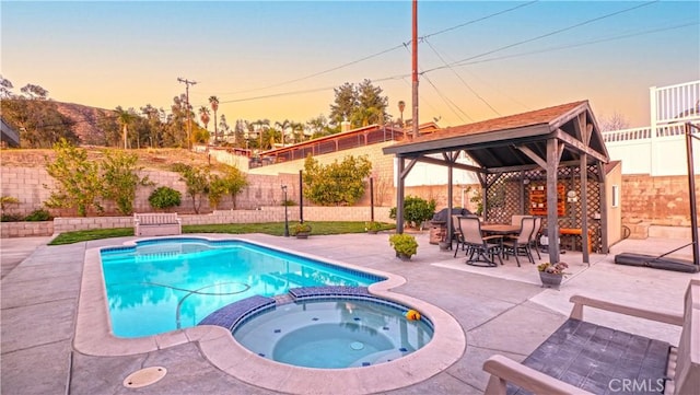 pool at dusk with a patio area, a pool with connected hot tub, a fenced backyard, and a gazebo