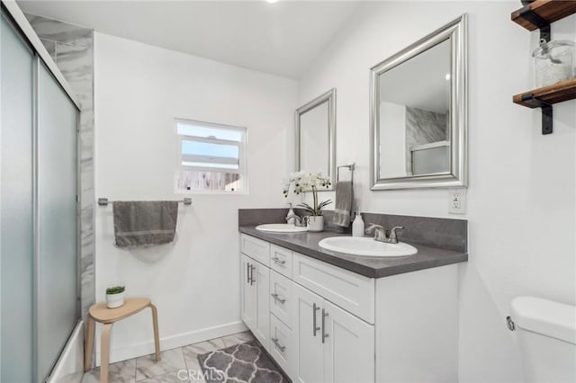 full bathroom featuring toilet, double vanity, a sink, and a shower with door