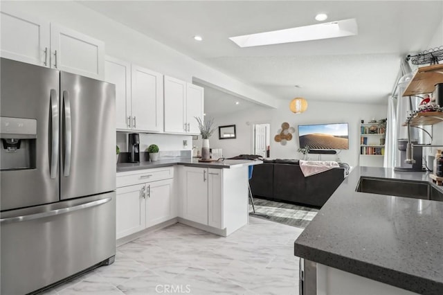 kitchen featuring vaulted ceiling with skylight, a peninsula, white cabinets, open floor plan, and stainless steel fridge