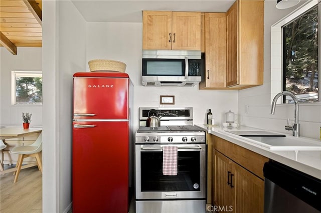 kitchen with a sink, stainless steel appliances, light countertops, light wood-type flooring, and beam ceiling