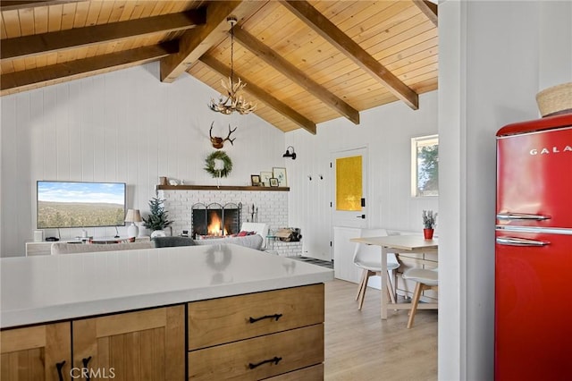 kitchen with lofted ceiling with beams, wooden ceiling, light wood-style flooring, freestanding refrigerator, and a brick fireplace