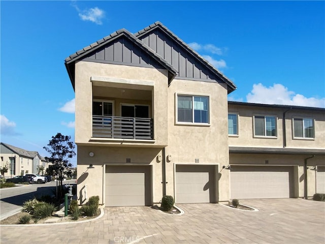 view of front facade featuring an attached garage, a balcony, decorative driveway, stucco siding, and board and batten siding