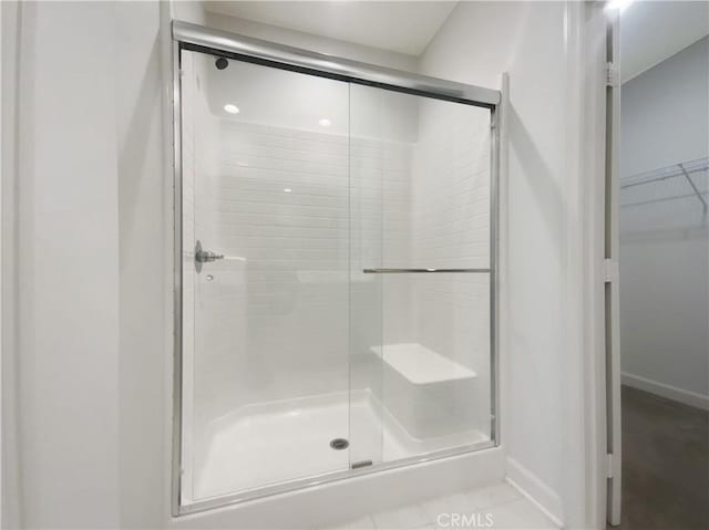 full bathroom with a spacious closet, a stall shower, and baseboards