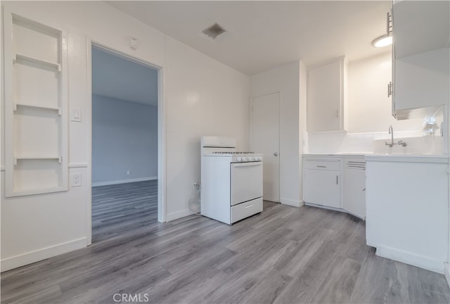 kitchen featuring gas range gas stove, light countertops, light wood-style floors, white cabinets, and baseboards