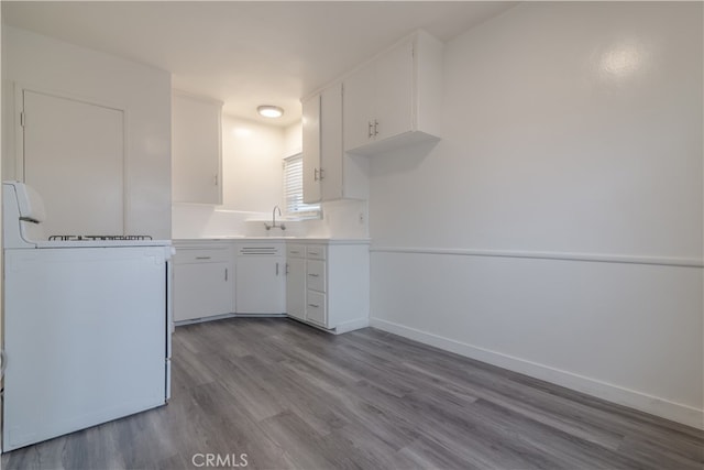 kitchen featuring baseboards, range, white cabinets, wood finished floors, and light countertops