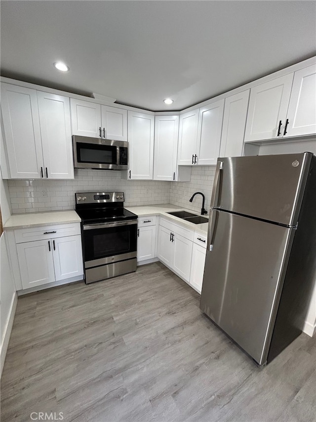 kitchen featuring light wood finished floors, appliances with stainless steel finishes, a sink, and white cabinets