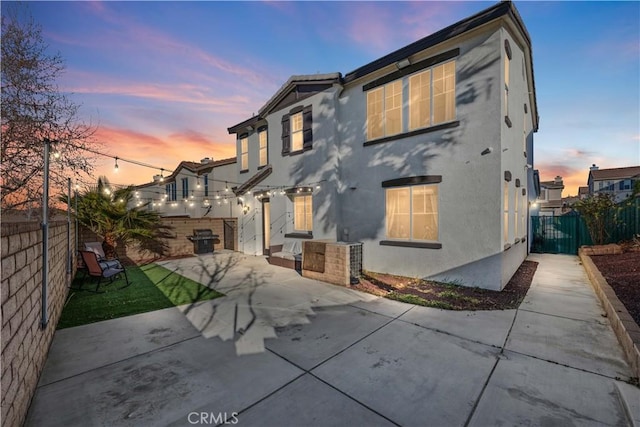 back of property at dusk featuring a patio area, a fenced backyard, and stucco siding