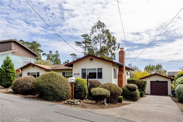 bungalow-style home featuring a garage, driveway, a chimney, an outdoor structure, and stucco siding