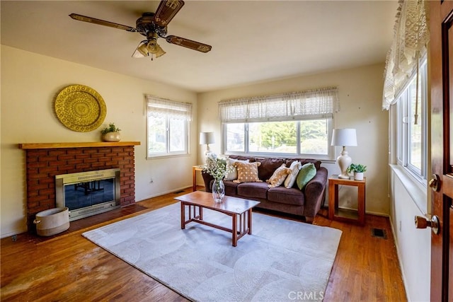 living area featuring a brick fireplace, wood finished floors, visible vents, and a healthy amount of sunlight