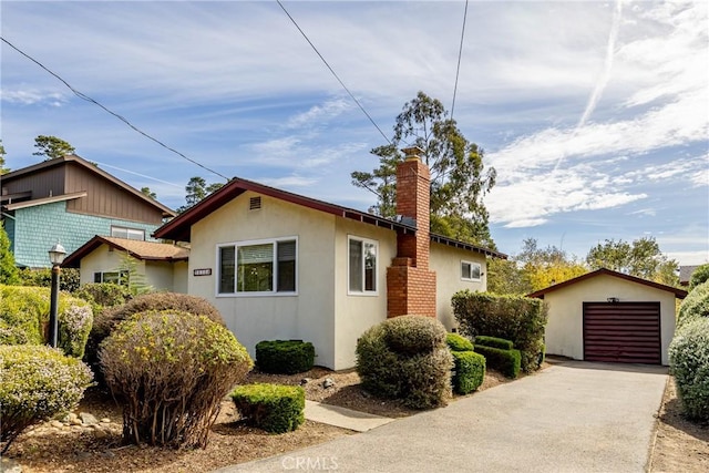 view of front of home with a garage, an outdoor structure, concrete driveway, stucco siding, and a chimney