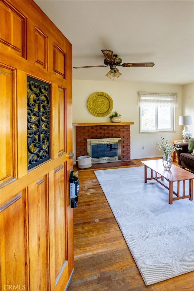 living area with ceiling fan, a fireplace, and wood finished floors