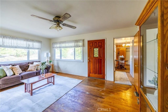 living area with ceiling fan with notable chandelier and wood finished floors