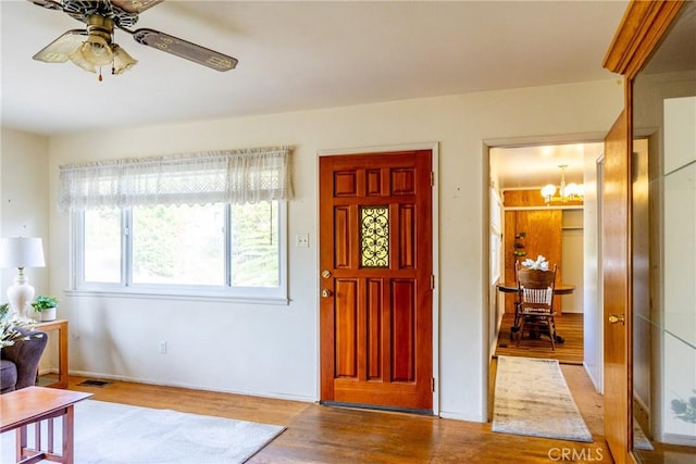 foyer entrance with ceiling fan with notable chandelier, wood finished floors, and visible vents