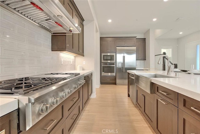 114 Source, Irvine, CA 92618 - kitchen featuring built in appliances, wall chimney range hood, light countertops, tasteful backsplash, and light wood-style flooring