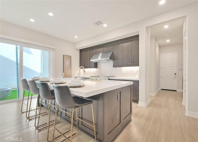 114 Source, Irvine, CA 92618 - kitchen with under cabinet range hood, decorative backsplash, a sink, a kitchen island with sink, and a kitchen bar