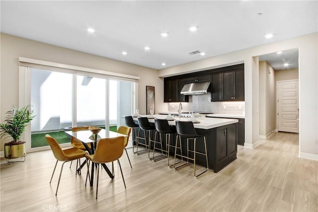 114 Source, Irvine, CA 92618 - kitchen with under cabinet range hood, light countertops, backsplash, light wood-style floors, and a breakfast bar area