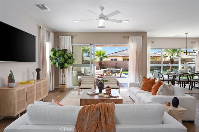 living area with ceiling fan with notable chandelier, visible vents, and wood finished floors