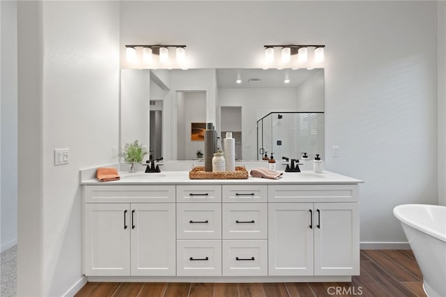 bathroom featuring double vanity, wood finished floors, a sink, and a shower stall