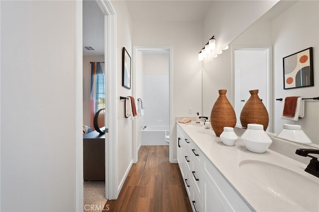 bathroom with a washtub, double vanity, visible vents, a sink, and wood finished floors