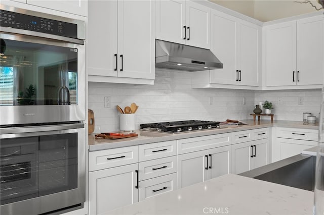 kitchen with white cabinets, decorative backsplash, appliances with stainless steel finishes, light stone countertops, and under cabinet range hood