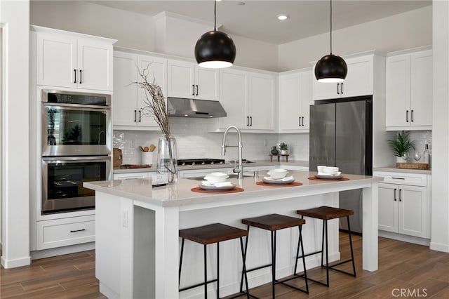 kitchen featuring dark wood-style floors, appliances with stainless steel finishes, light countertops, under cabinet range hood, and backsplash