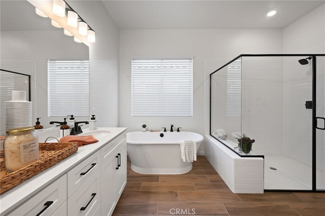 full bathroom featuring wood finish floors, recessed lighting, a stall shower, vanity, and a freestanding tub