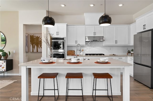 kitchen with stainless steel appliances, a breakfast bar area, backsplash, and under cabinet range hood