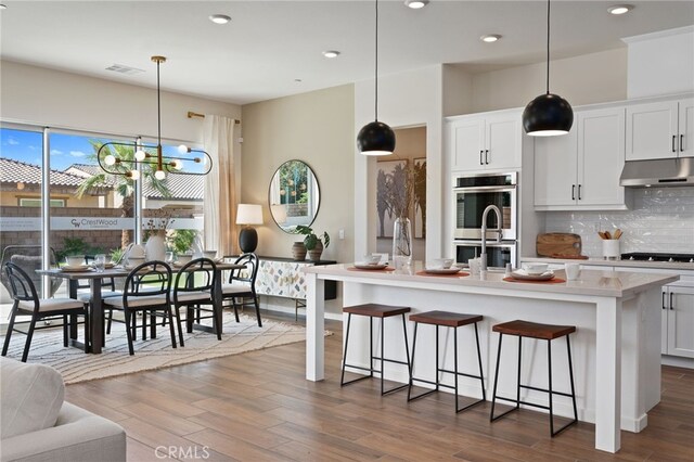 kitchen featuring under cabinet range hood, double oven, visible vents, and dark wood-style flooring