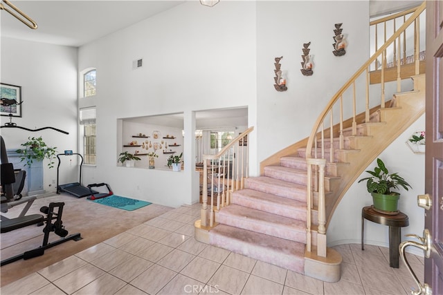 carpeted foyer entrance with stairway, tile patterned flooring, a high ceiling, and visible vents