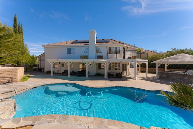 rear view of property featuring solar panels, a chimney, a patio area, and an outdoor pool