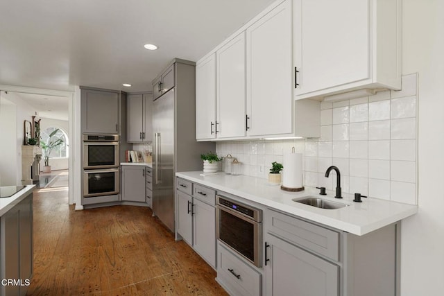 kitchen featuring gray cabinetry, tasteful backsplash, wood finished floors, stainless steel appliances, and light countertops