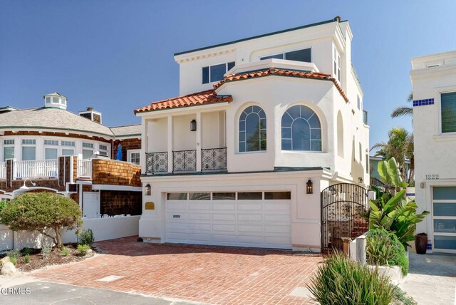 mediterranean / spanish house featuring decorative driveway, a garage, a balcony, and stucco siding