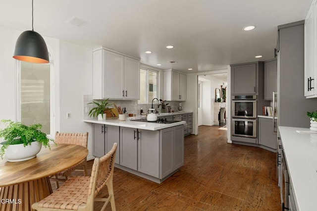 kitchen with dark wood-type flooring, gray cabinets, double oven, a peninsula, and light countertops