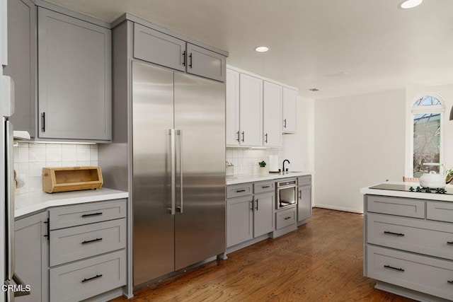 kitchen with light countertops, stainless steel built in refrigerator, wood finished floors, and gray cabinetry