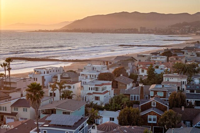 aerial view at dusk with a residential view, a view of the beach, and a water and mountain view