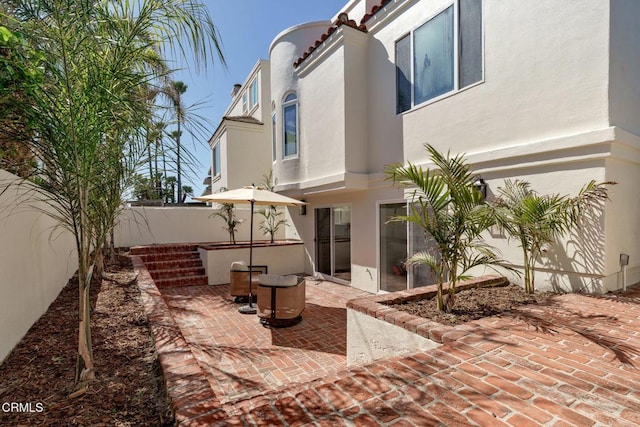 rear view of property with stucco siding, a patio, a tile roof, and fence