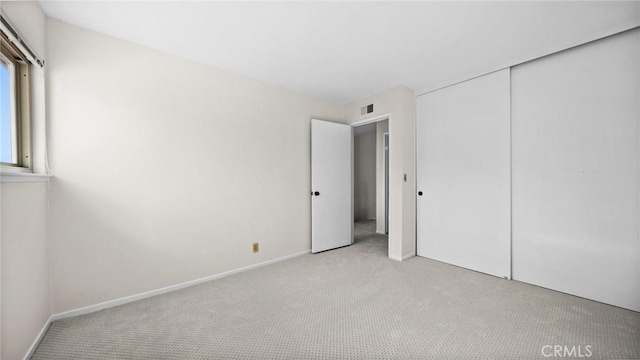 unfurnished bedroom with a closet, light colored carpet, visible vents, and baseboards